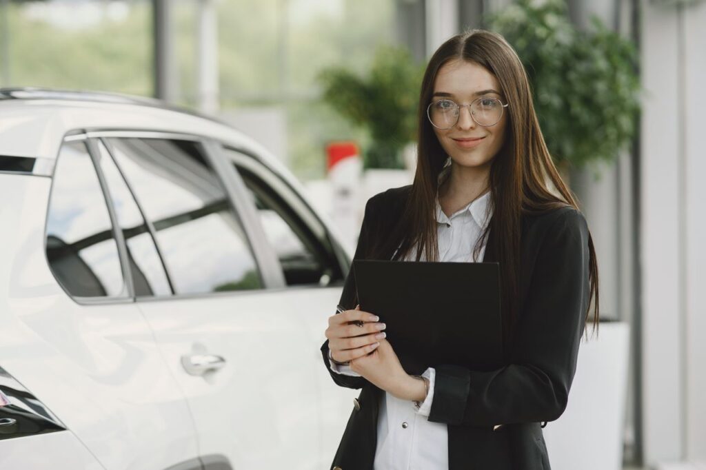 Businesswoman with a clipboard standing beside a car in a modern showroom.